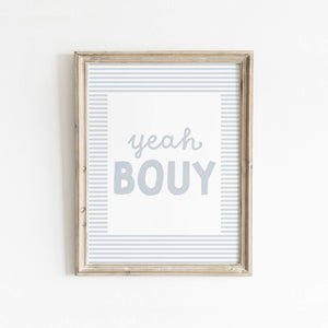 Yeah Bouy text art print in soft blue with striped border, framed in wood and styled against a clean white wall—perfect for beachy or coastal-inspired decor