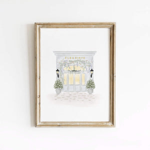 Fleuriste art print featuring a soft Parisian flower shop illustration, framed in light wood and styled against a white wall for elegant home decor.