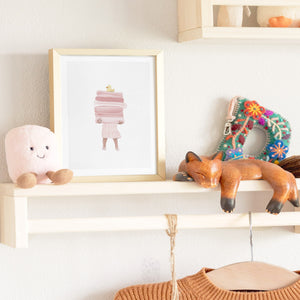 Framed girl bathroom art print on a shelf, styled with natural light and soft beige accents in a kids room setting.