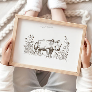 Baby rhino nursery wall art held by child, featuring a hand-drawn safari animal illustration in sepia tones for neutral kids’ room decor.