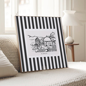 Oia Santorini printable art resting on a textured cream sofa, showing bold striped border and hand-drawn dome architecture in a cozy neutral space.