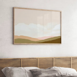 Soft-toned landscape art print with muted green and peachy pink hills, styled above a cane headboard in a cozy neutral bedroom.