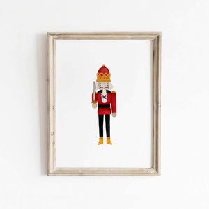 Nutcracker soldier wall art print with bold red uniform and gold crown, displayed in a natural wood frame for festive Christmas home decor.