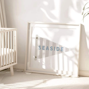 Seaside flag wall art print leaning against a nursery wall, styled with soft shadows and natural light. Perfect for coastal-inspired baby or kids' room decor.
