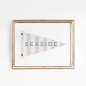 Minimalist Seaside flag art print framed in distressed wood, featuring soft blue text and neutral tones. Ideal for beach house or nautical-themed spaces.