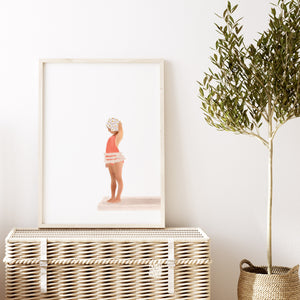 Framed girl diving board print styled above a woven bench with soft white walls and natural textures, perfect for a coastal kids bathroom or nursery.