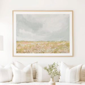 Horizontal meadow artwork in a natural wood frame hung above neutral sofa with linen textures and soft daylight.