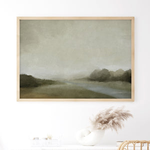 Framed moody landscape print with soft green tones and overcast sky, styled above a console with neutral decor and pampas grass.
