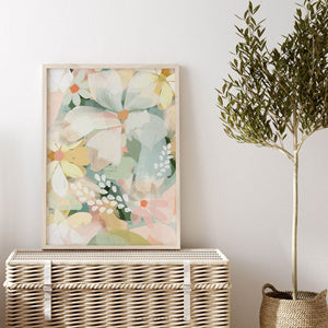 Framed abstract daisy print leaning on a rattan chest, styled with an olive tree and white wall – pastel floral wall art for modern spaces.