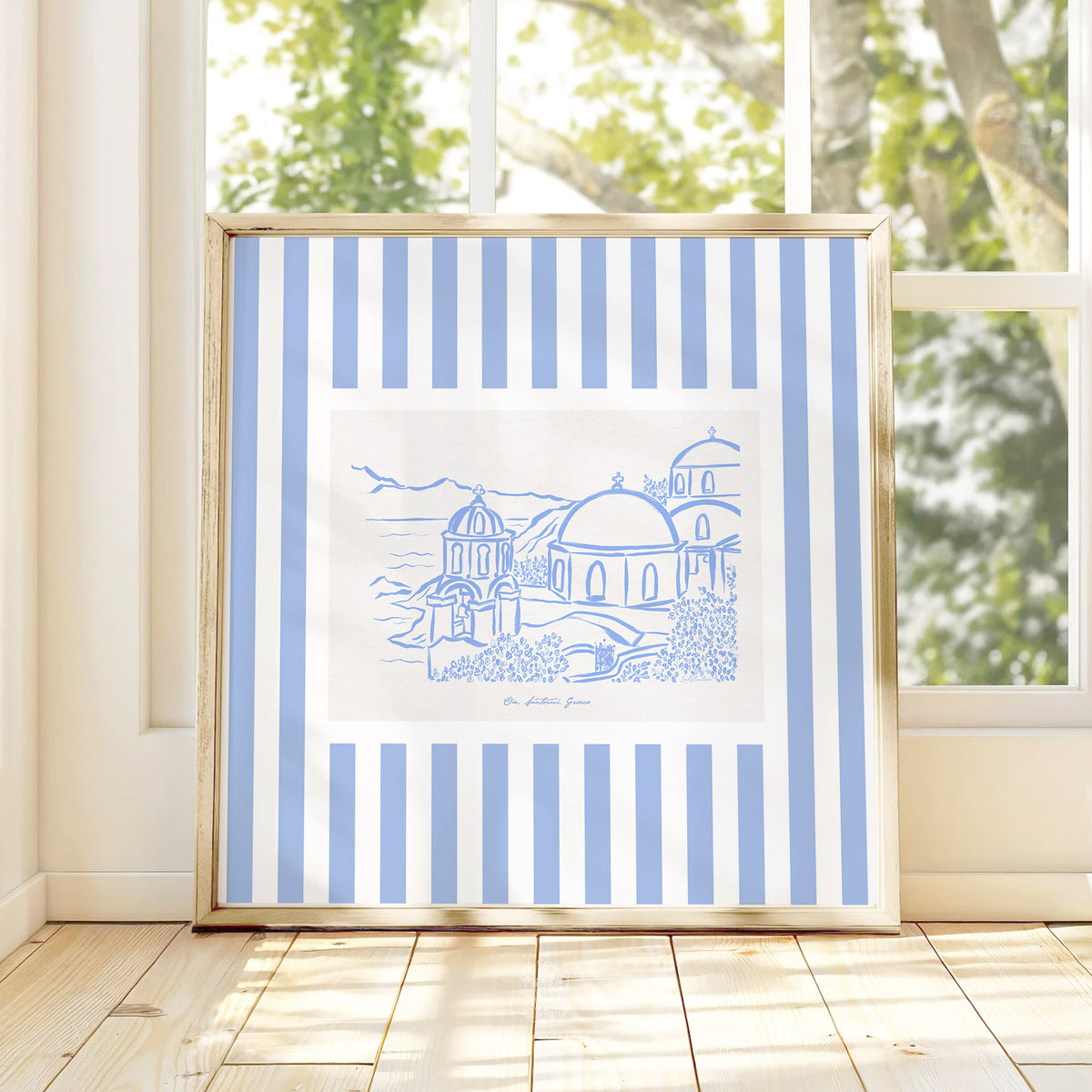 Modern Greece travel artwork leaning in a sunlit room, featuring blue and white striped border and hand-drawn island architecture.