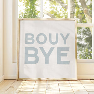 Framed blue and white typography art print with the words “BOUY BYE," styled in natural light on wood flooring.