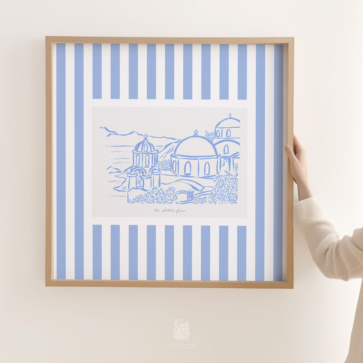 Blue and white Santorini sketch print being hung on a neutral wall, showing modern travel-inspired art with classic coastal tones.