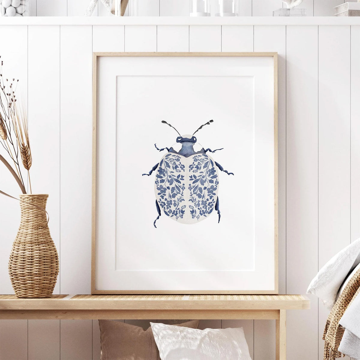 Blue and white insect art print framed in light wood, styled in a cozy neutral room with soft textures. Perfect for modern gallery walls or nature-themed decor.