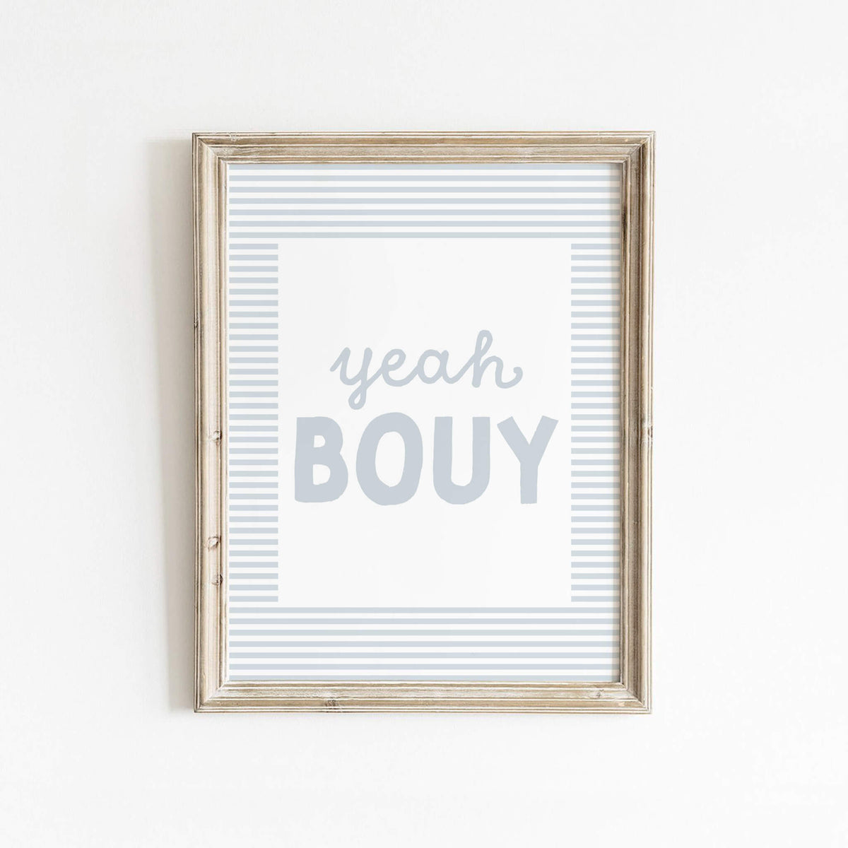 Yeah Bouy text art print in soft blue with striped border, framed in wood and styled against a clean white wall—perfect for beachy or coastal-inspired decor