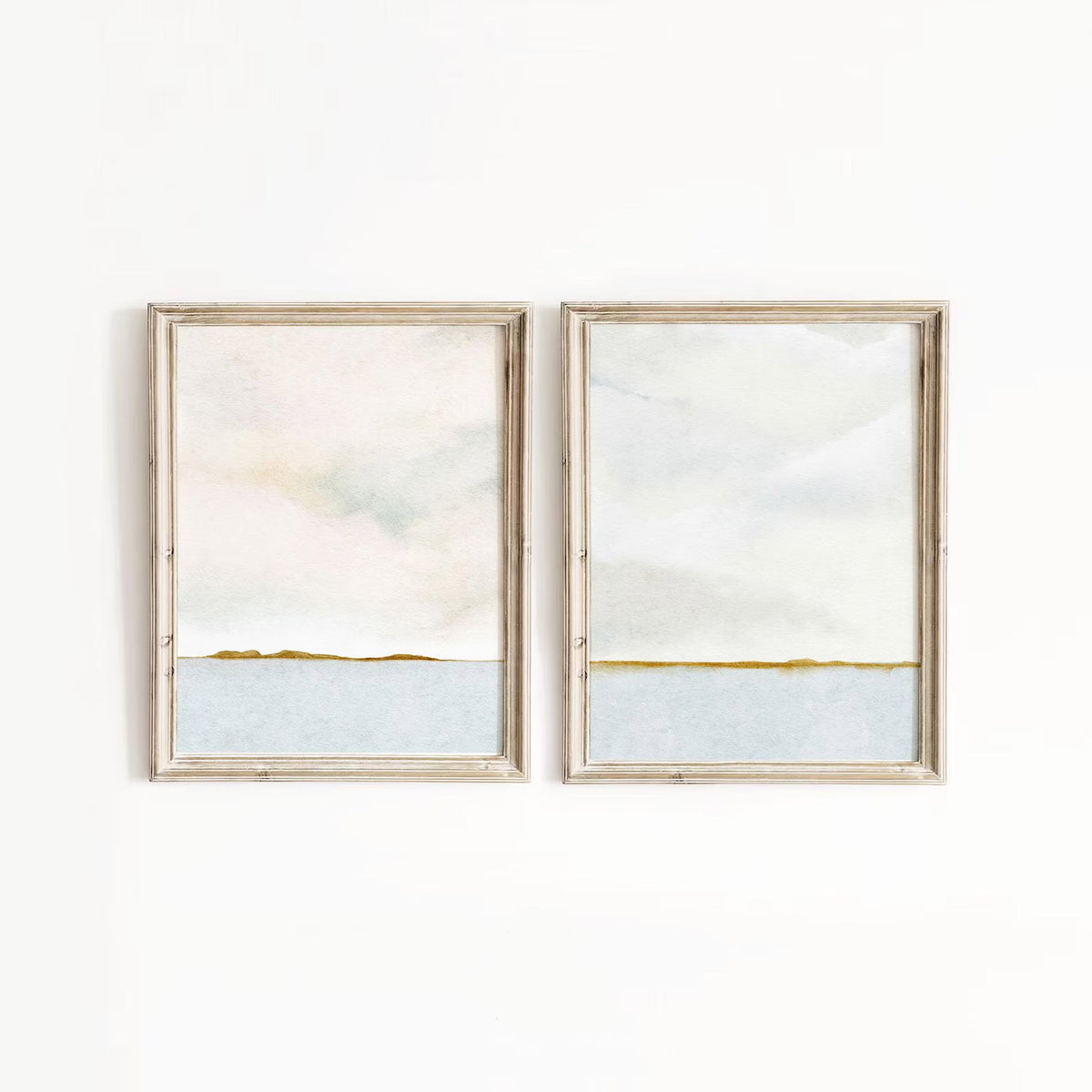 A pair of minimalist ocean horizon prints with delicate gold-green toned detailing, hung on a bedroom wall for effortless styling.