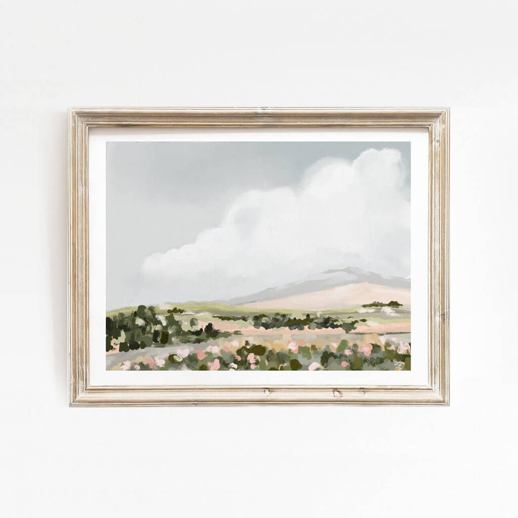 Soft countryside landscape print framed on a white wall, featuring gentle brushstrokes, earthy tones, and cloudy skies—perfect for adding calm to living rooms or bedrooms.