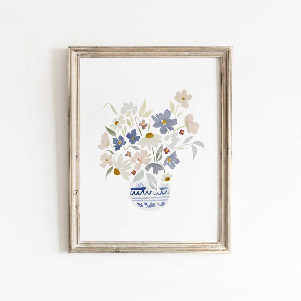 Framed floral wall art print with soft pink, blue, and sage wildflowers in a blue vase, styled for bedrooms, hallways, or transitional spaces.