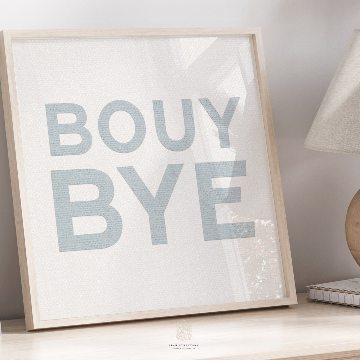 Playful blue coastal art print with “BOUY BYE” text, styled in a cozy neutral space with natural wood accents.