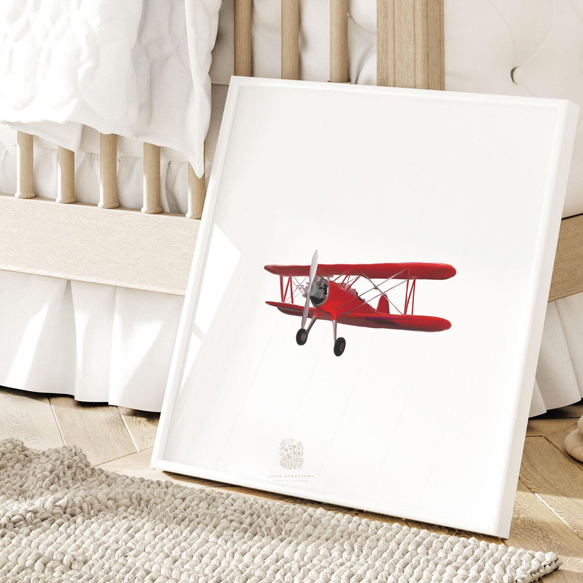 Framed red vintage biplane wall art styled in a nursery, leaning near crib for classic aviation-themed kids room or baby boy decor.