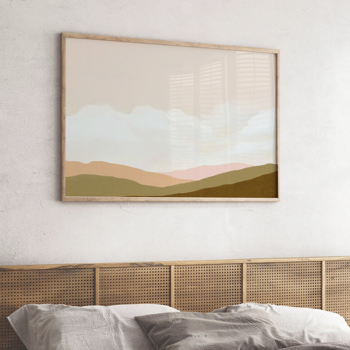 Soft-toned landscape art print with muted green and peachy pink hills, styled above a cane headboard in a cozy neutral bedroom.