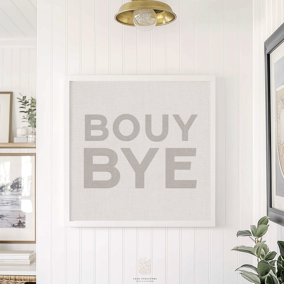 Modern neutral coastal art print reading “BOUY BYE,” framed in white and styled in a bright hallway with botanical accents.