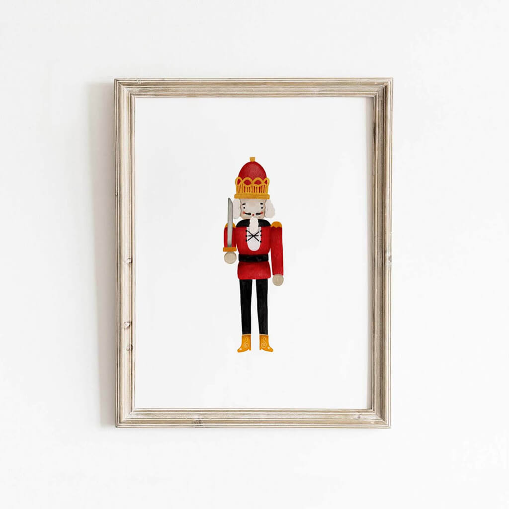 Nutcracker soldier wall art print with bold red uniform and gold crown, displayed in a natural wood frame for festive Christmas home decor.