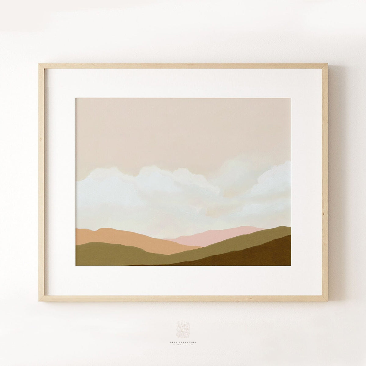 Framed landscape wall art featuring calming layered hills and cloudy sky in earthy tones, shown against a white wall.