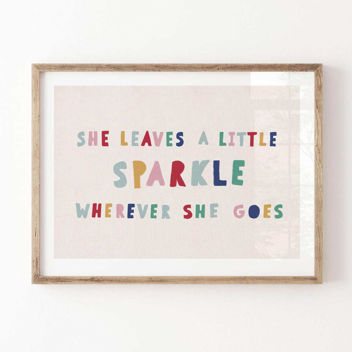 Close-up of colorful hand-lettered quote print in a rustic wood frame against a white wall, with soft shadows highlighting linen-style texture.