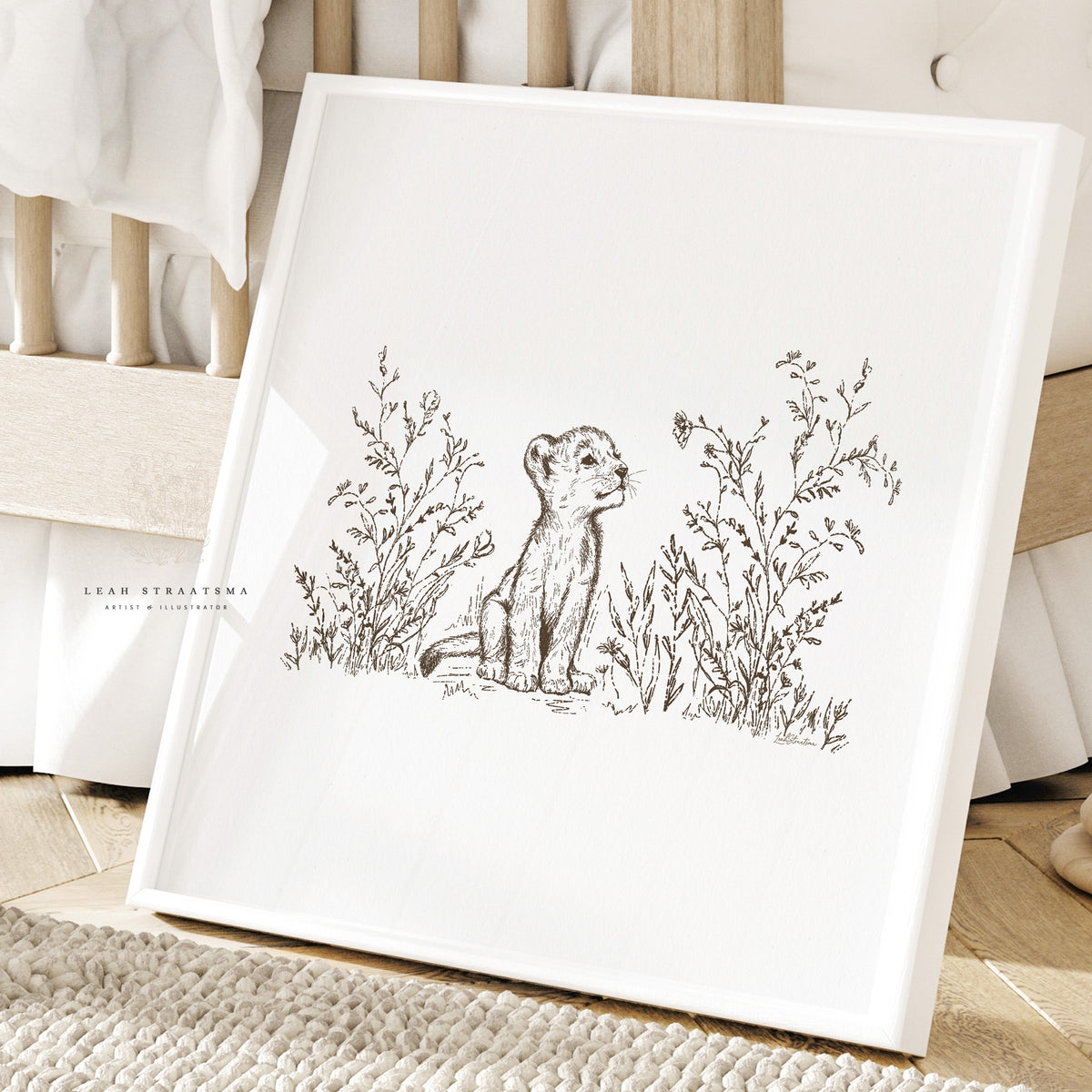 Lion cub safari nursery print in white frame, shown leaning against a crib with natural wood and cozy textures in a neutral baby space.