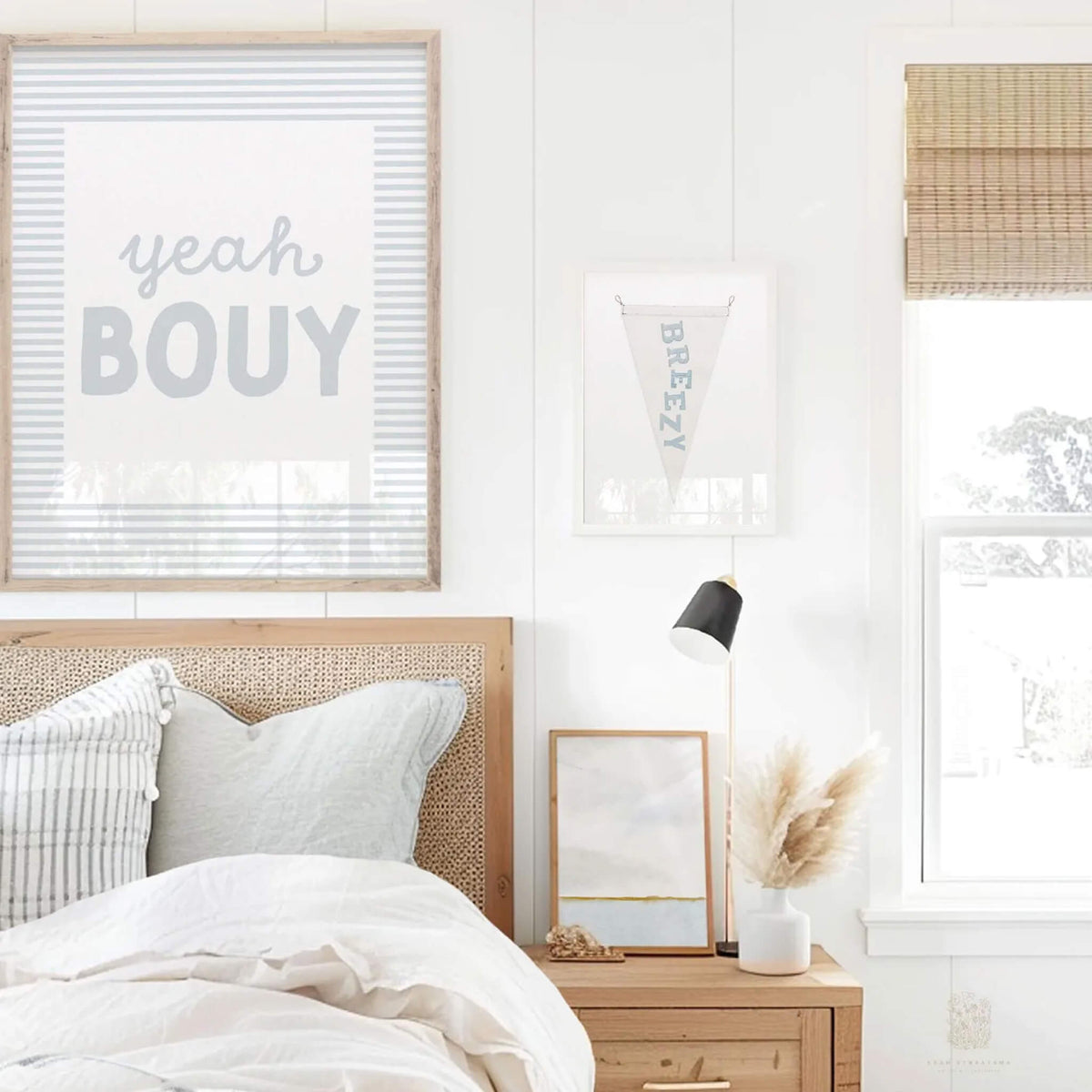 Yeah Bouy wall art print framed above bed with cane headboard and light coastal decor, styled next to Breezy pennant for playful beach house vibes.