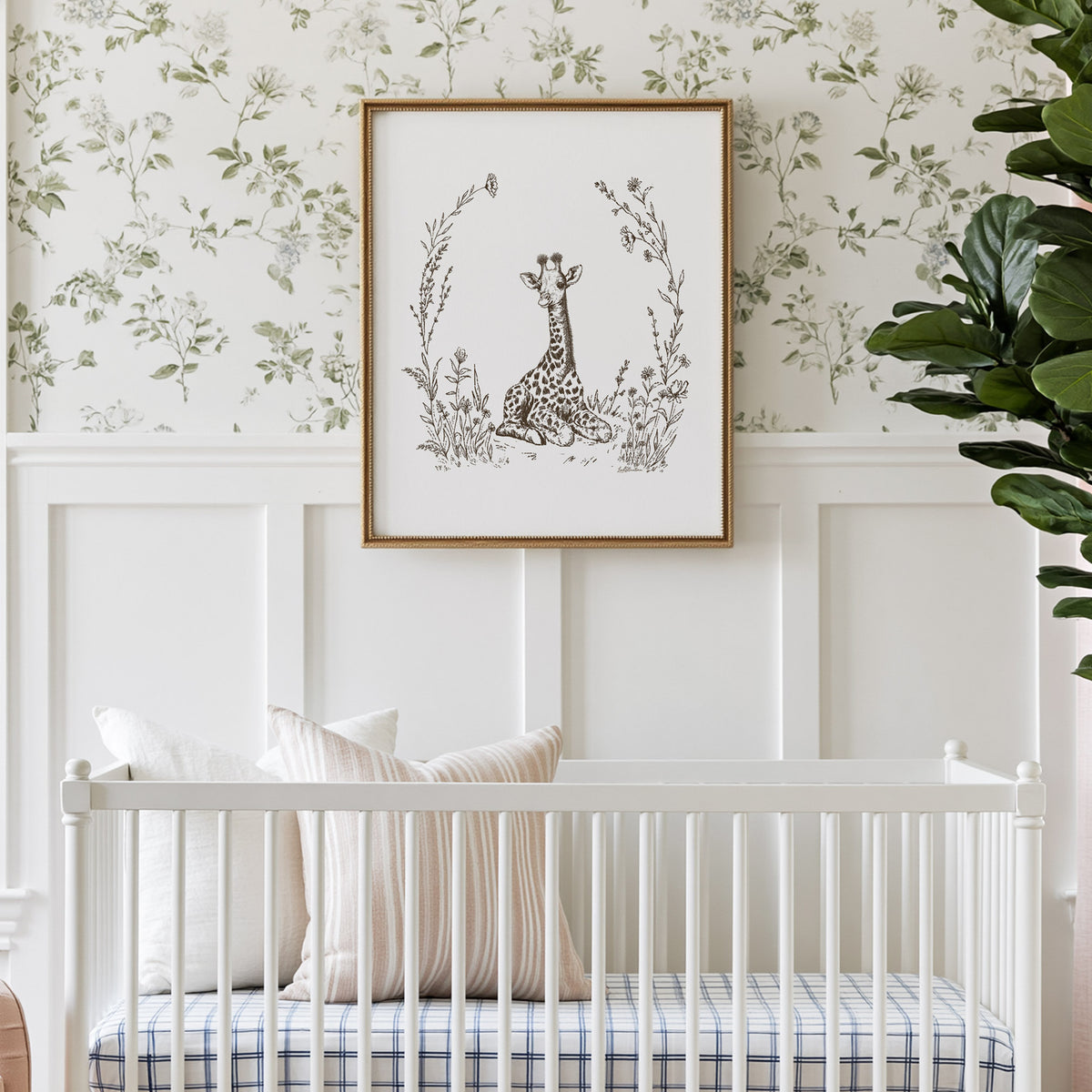 Baby giraffe print with delicate wildflowers and grasses, displayed in a gold frame above a white crib in a botanical nursery.