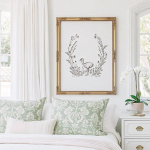 Baby Ostrich Print featuring a hand-drawn ostrich surrounded by delicate wildflowers, displayed in an ornate gold frame above a bed.