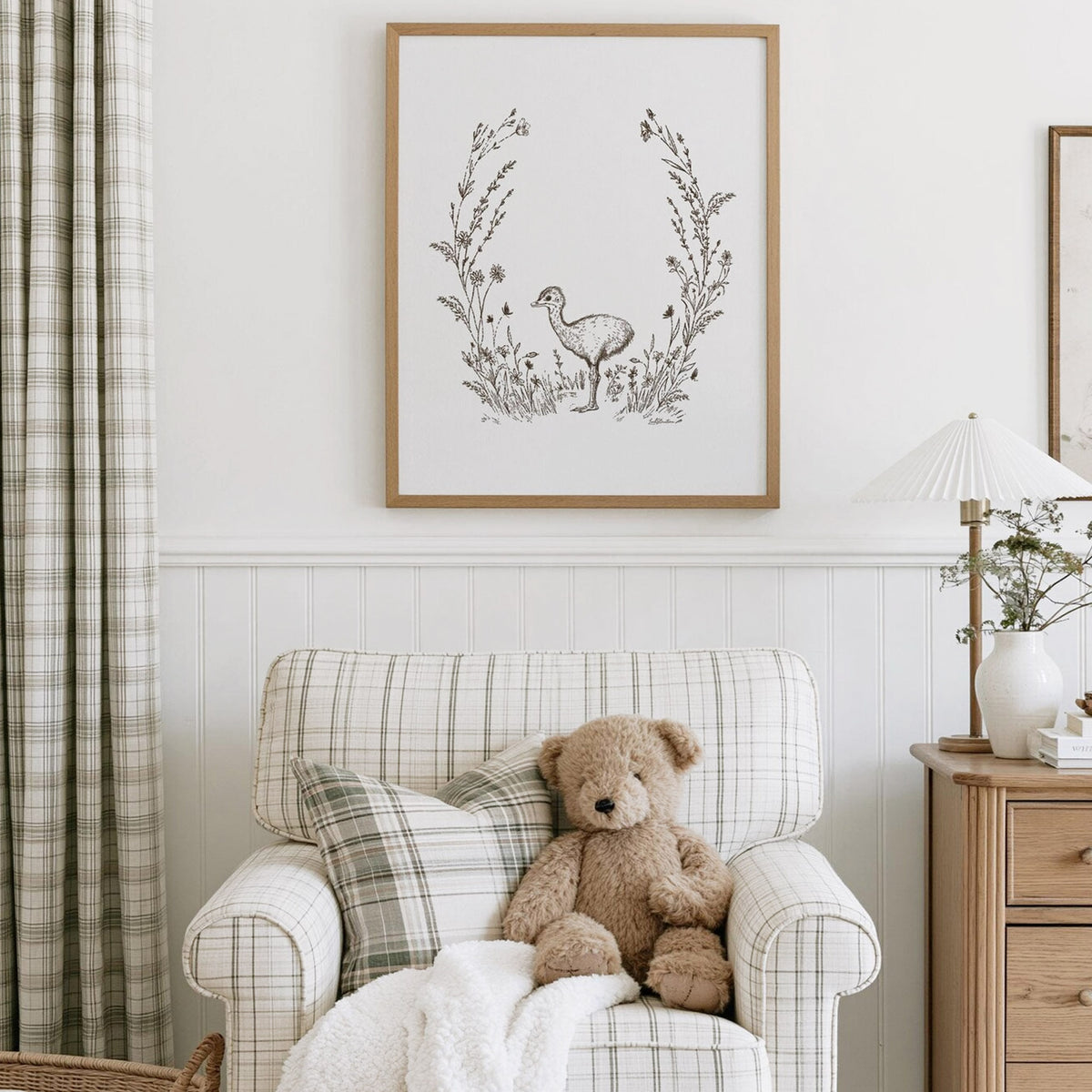 Baby Ostrich Print with delicate wildflowers and grasses, displayed in a natural wood frame above a plaid nursery chair with a teddy bear.