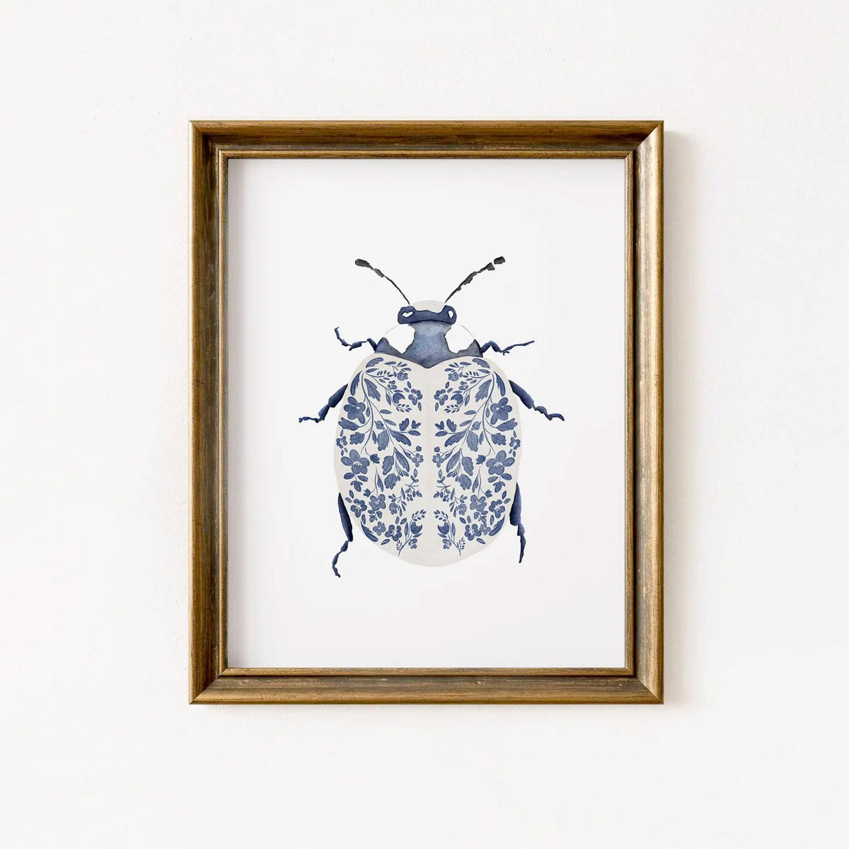 Blue Ladybug Print featuring a navy and white beetle with delicate floral-patterned wings, displayed in a simple bronze gold frame.