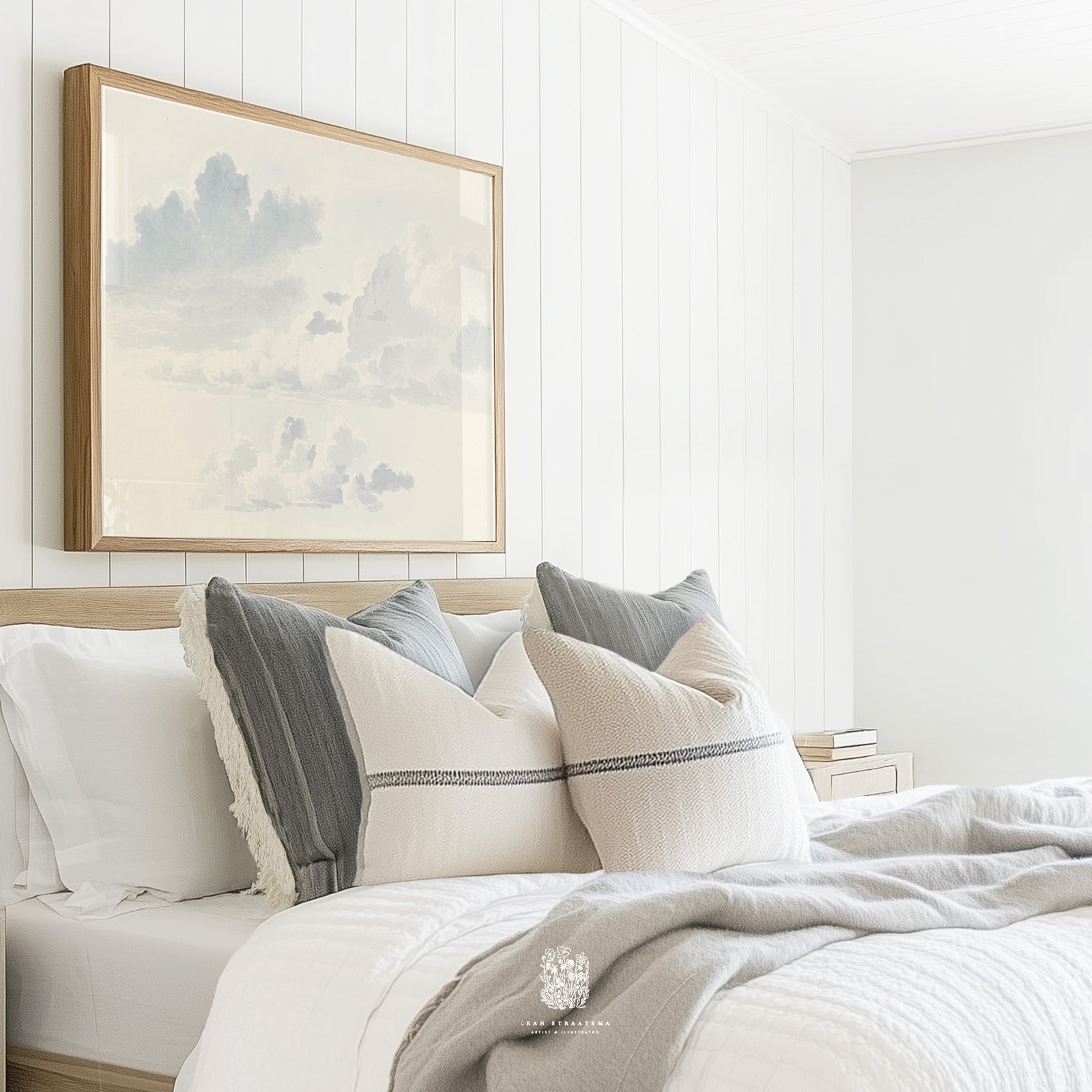 Framed cloud wall art above a neutral-toned bed with layered pillows and shiplap walls, styled for a calm, modern bedroom.
