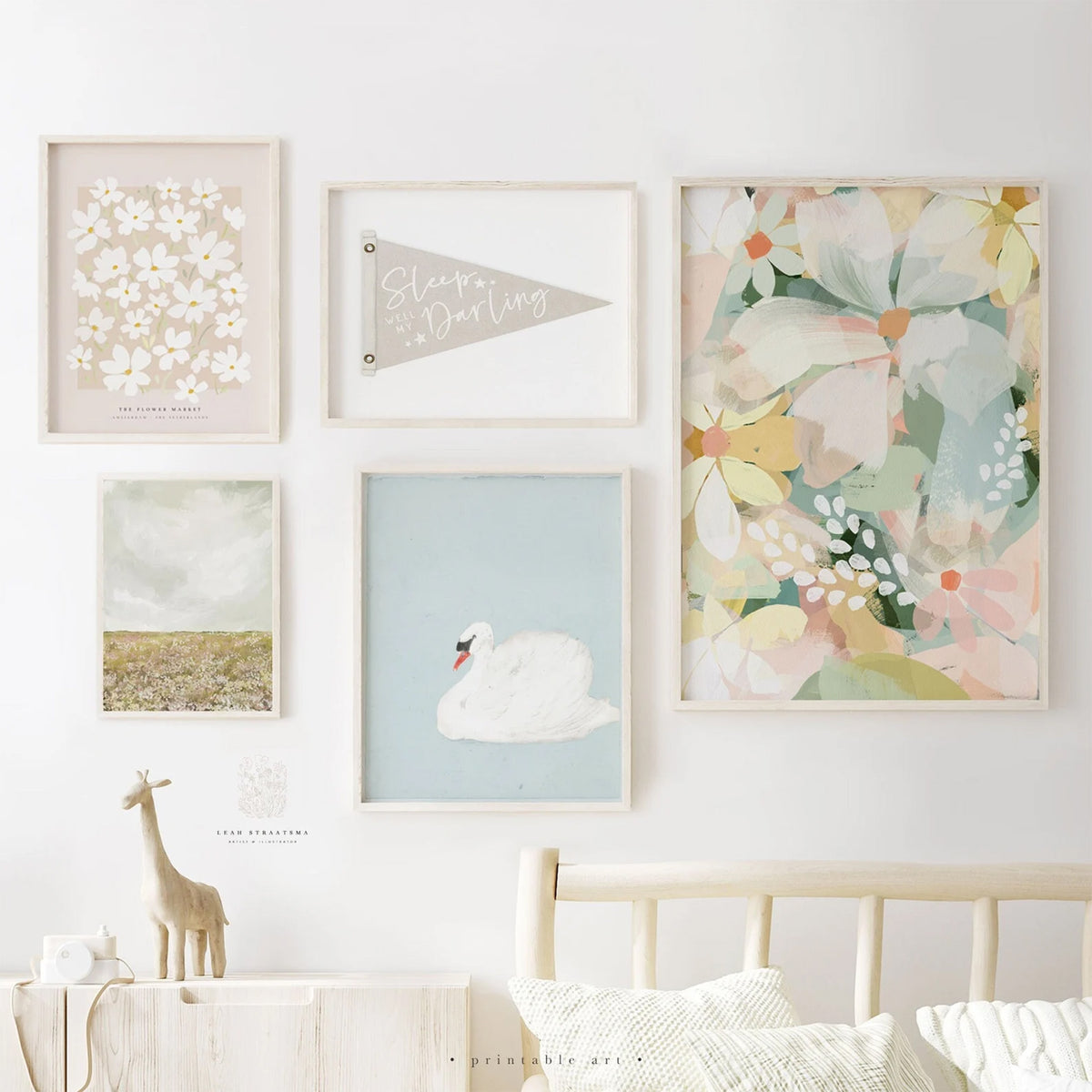 Framed gallery wall featuring five printable art pieces including florals, a swan, a pennant, and soft landscape, styled for a girls nursery or bathroom.