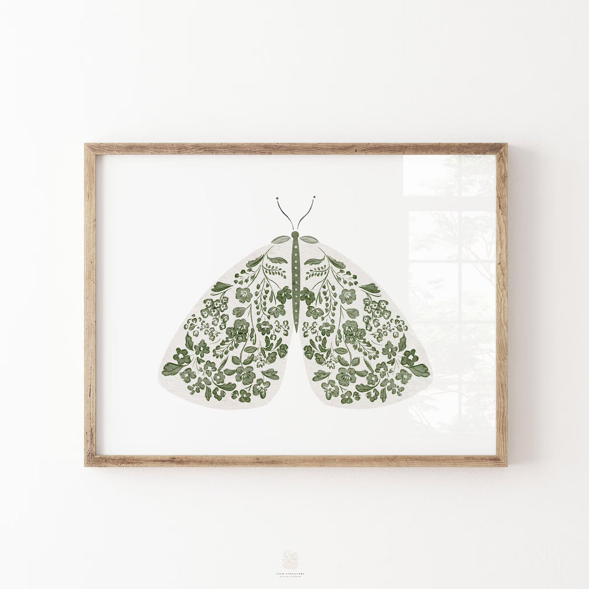 Green moth print with intricate flowers and leafy botanical details across its wings, displayed in a natural wood frame on a white wall.