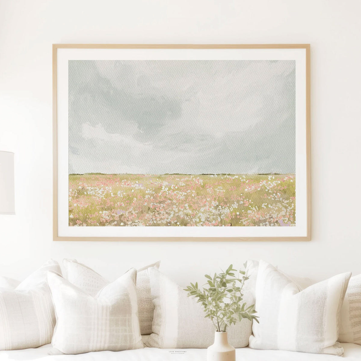 Horizontal meadow artwork in a natural wood frame hung above neutral sofa with linen textures and soft daylight.