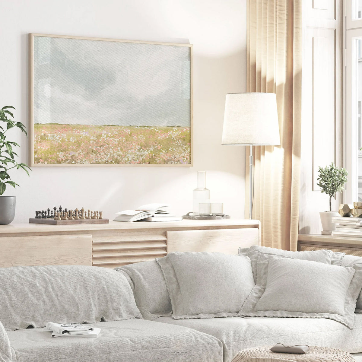 Framed pastel landscape art showing a field of tiny flowers beneath a cloudy sky, styled in a living room.