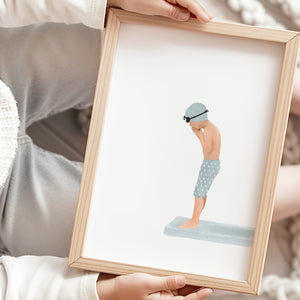 Child holding framed swimming artwork of a boy on a diving board, shown in soft neutral tones with rattan and linen textures.