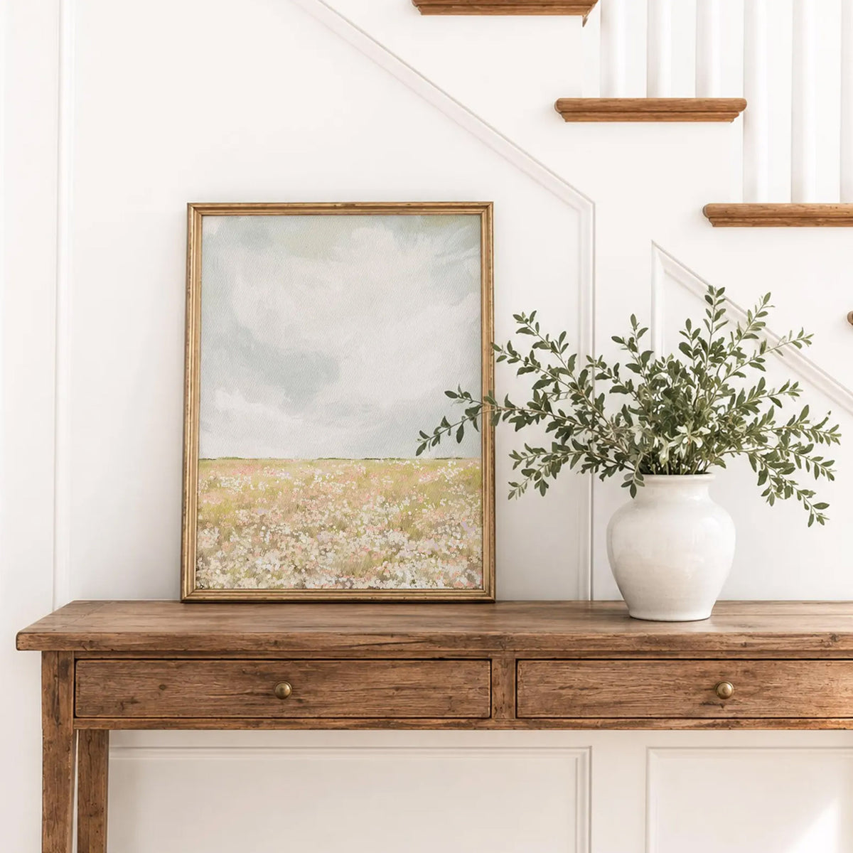 Wildflower Meadow Print with pastel flowers and a pale blue-grey sky, displayed in a gold frame on a wooden console table.